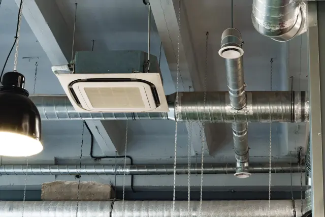 Deckenmontierte Lüftungsanlage mit Kassettengerät, runden verzinkten Luftkanälen und T-Stück in einem Gewerberaum, aus der Untersicht aufgenommen.