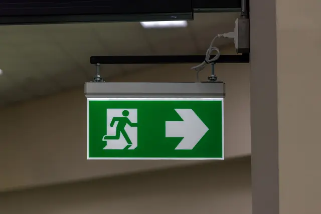 Grünes Notausgangsschild mit laufender Person und weißem Pfeil nach rechts, an einer Innenwand montiert.